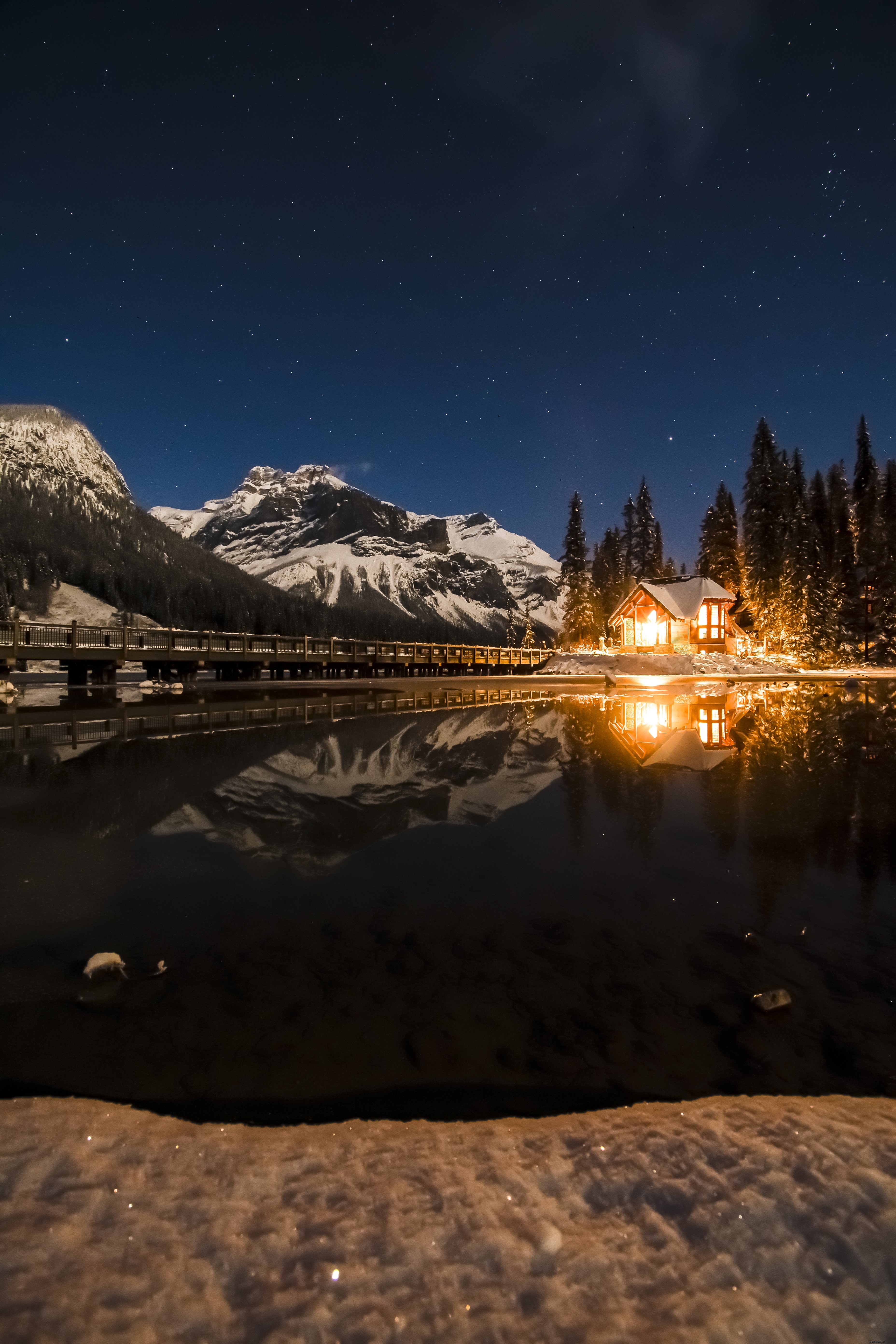 Stunning Winter Photo: Fire-Lit Cabin Glows by Frosty Lake Under Starry Sky