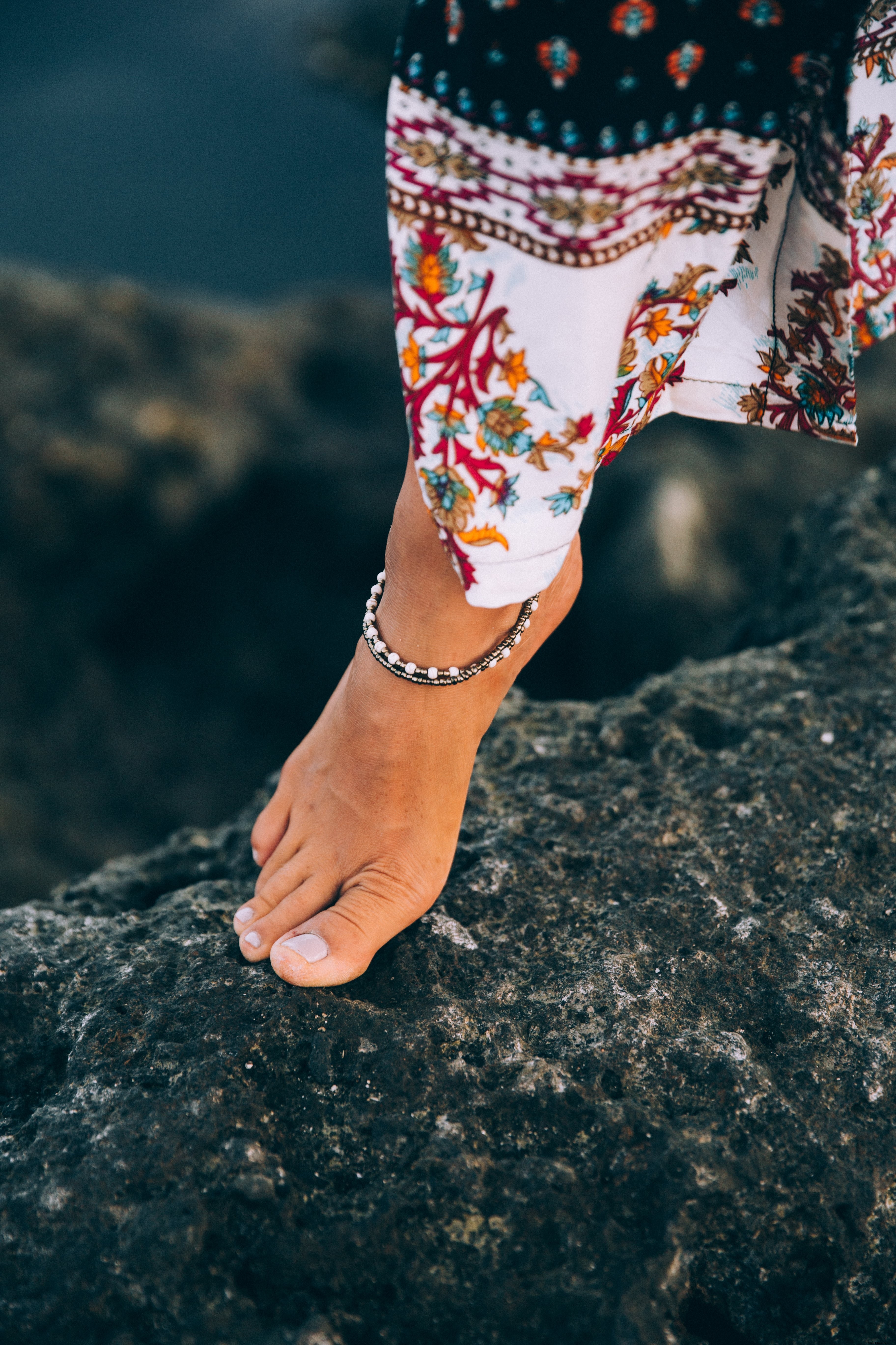 Stunning Tanned Woman Showcasing Anklet on Rocky Seashore – Captivating Beach Photo