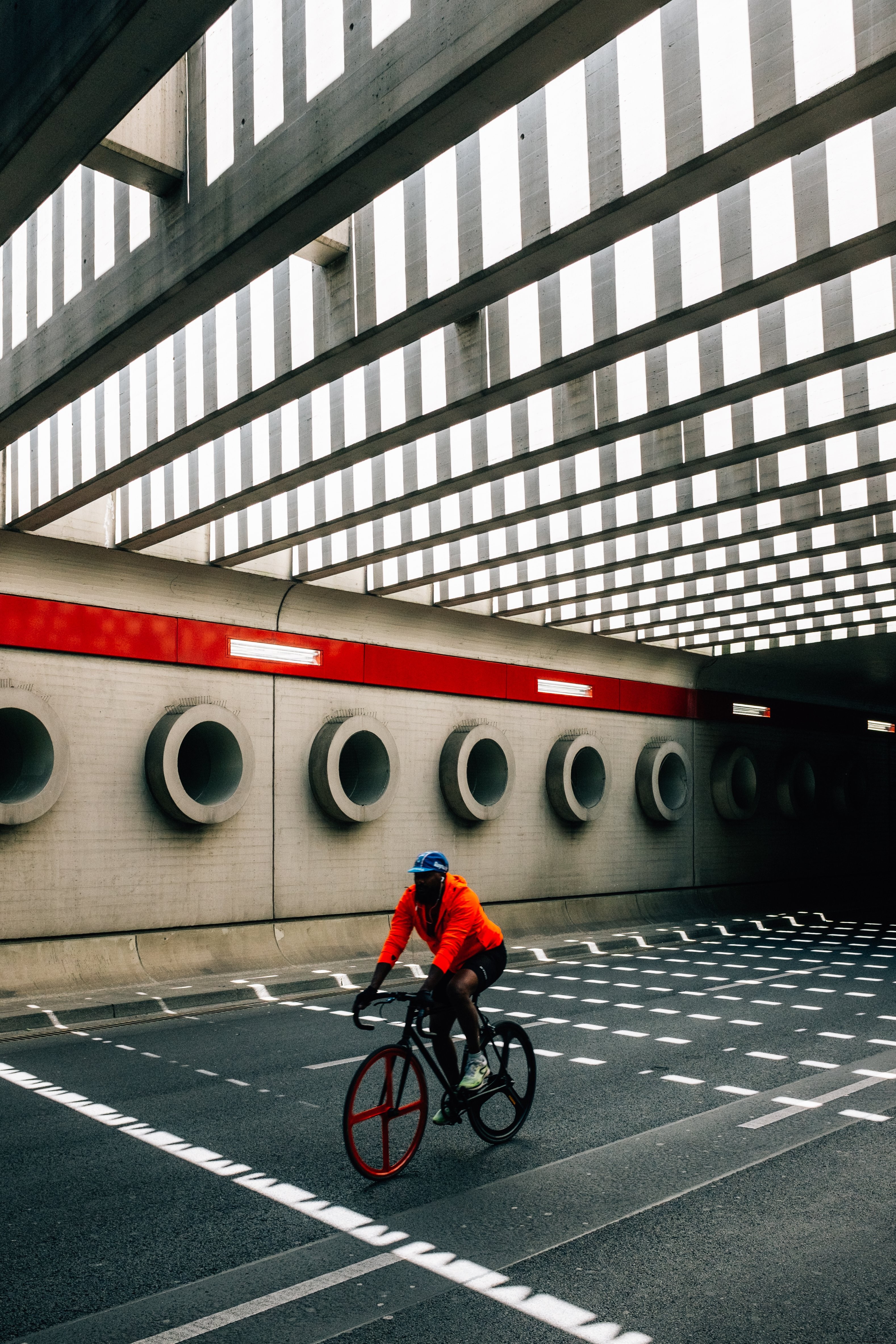 Dynamic Cyclist in Orange Rides Bike Under Urban Bridge – Stunning Photo