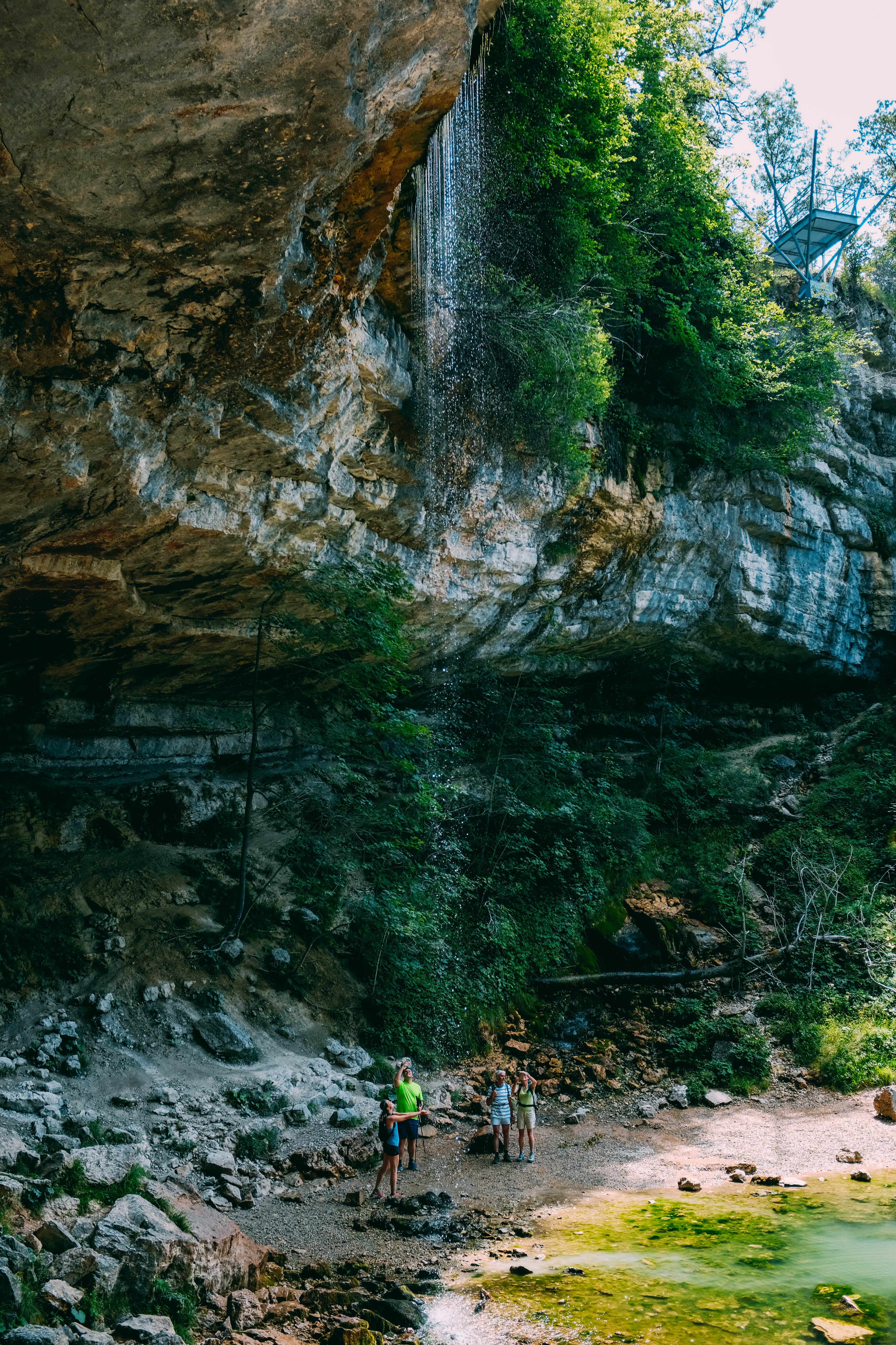 Stunning Photo of Hikers Beneath Rocky Outcrop and Cascading Waterfall