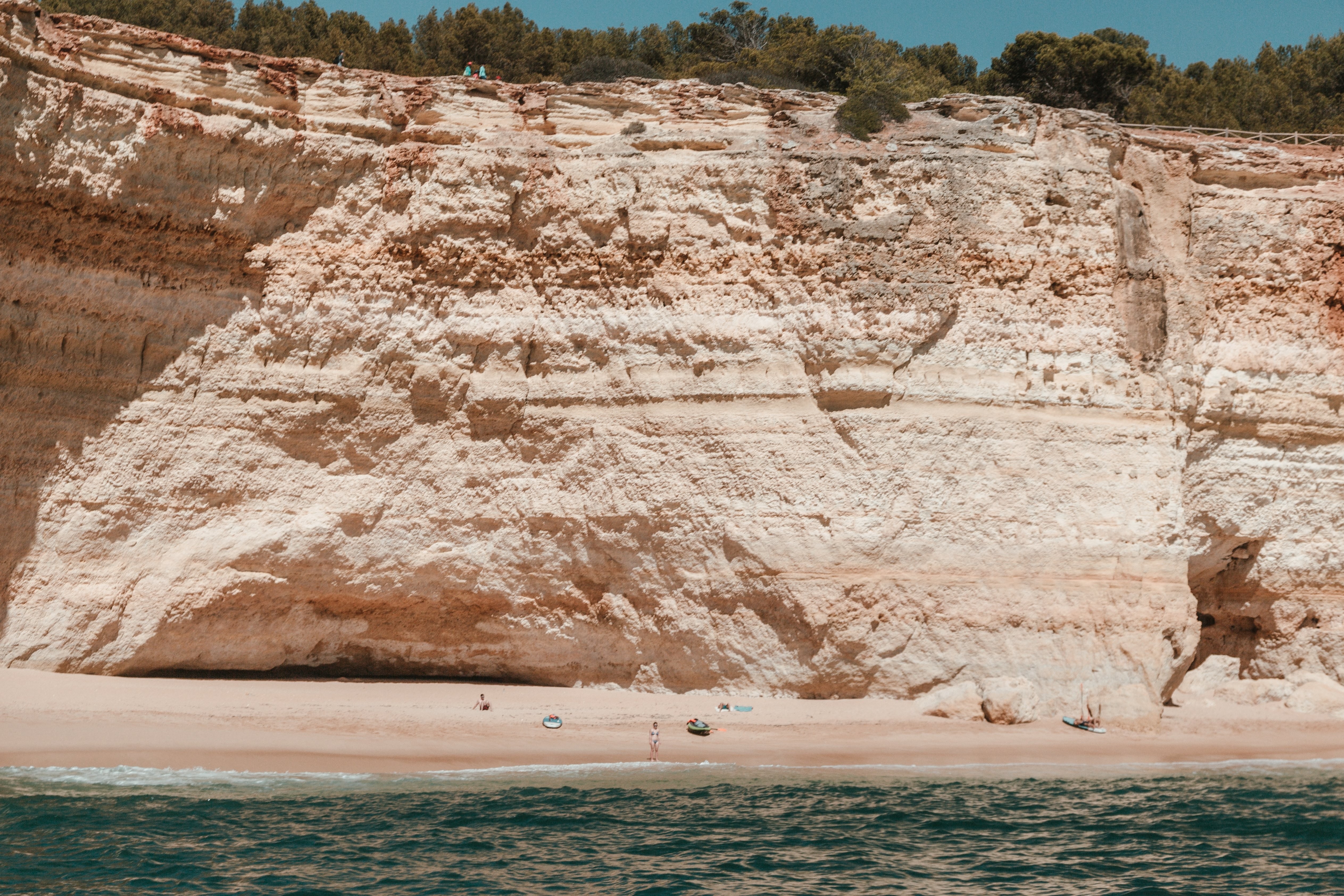 Stunning Photo: Kayakers and Surfers on Sandy Beach Under Towering Limestone Cliffs