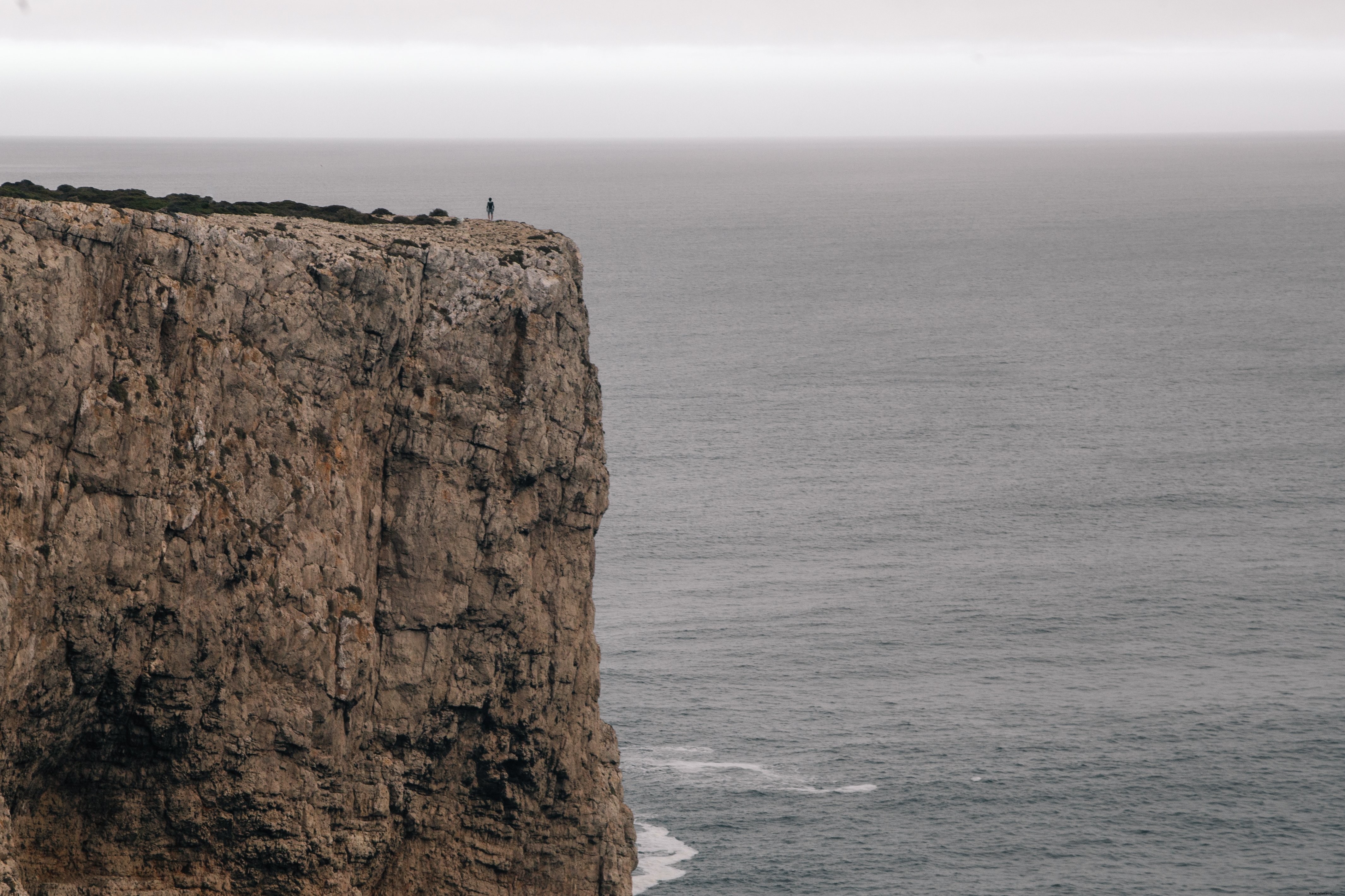 Dramatic Photo: Solitary Figure on Cliff Overlooking Ocean Under Gray Sky