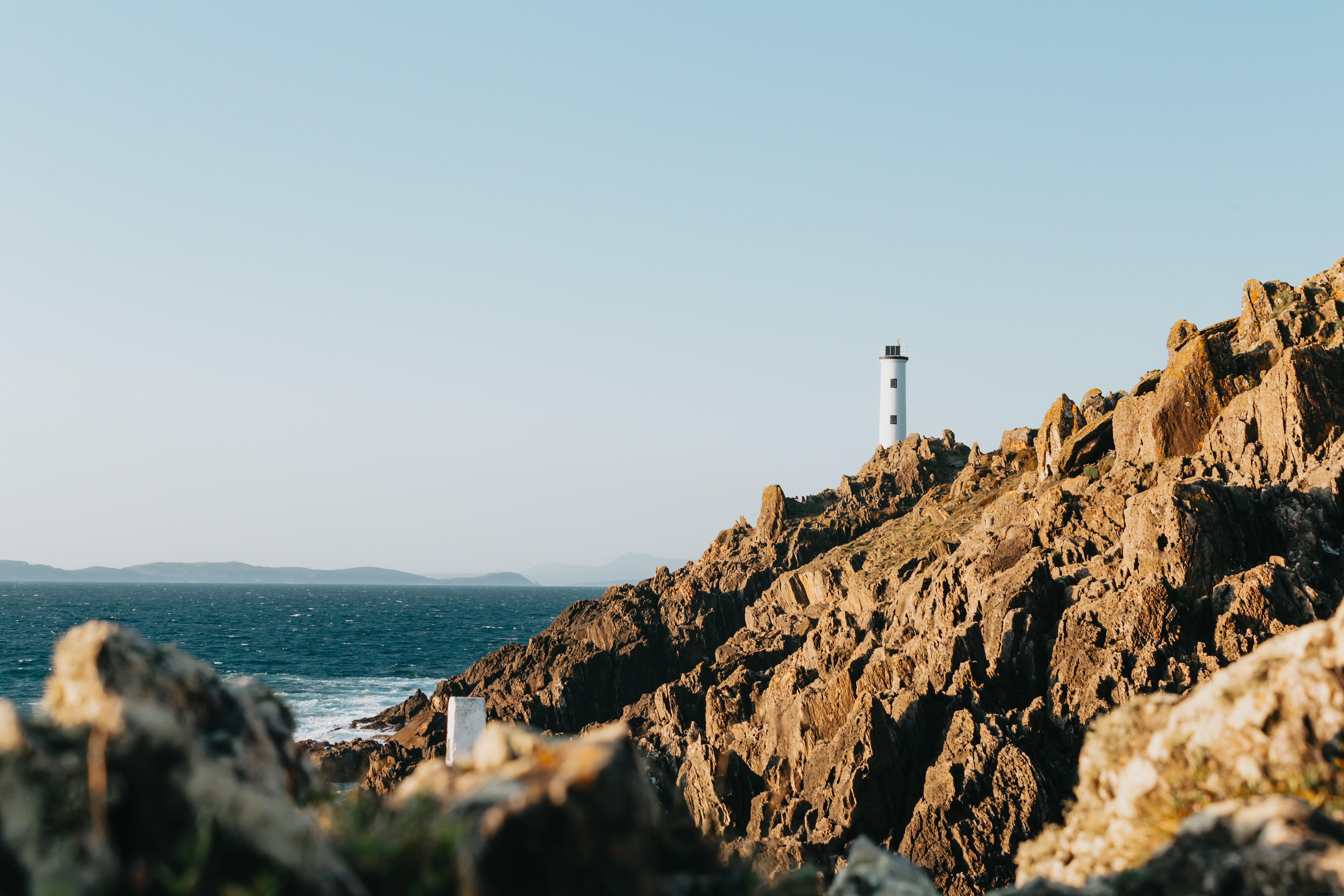 Majestic Tall Lighthouse on Rugged Rocky Shoreline Against Azure Blue Waters