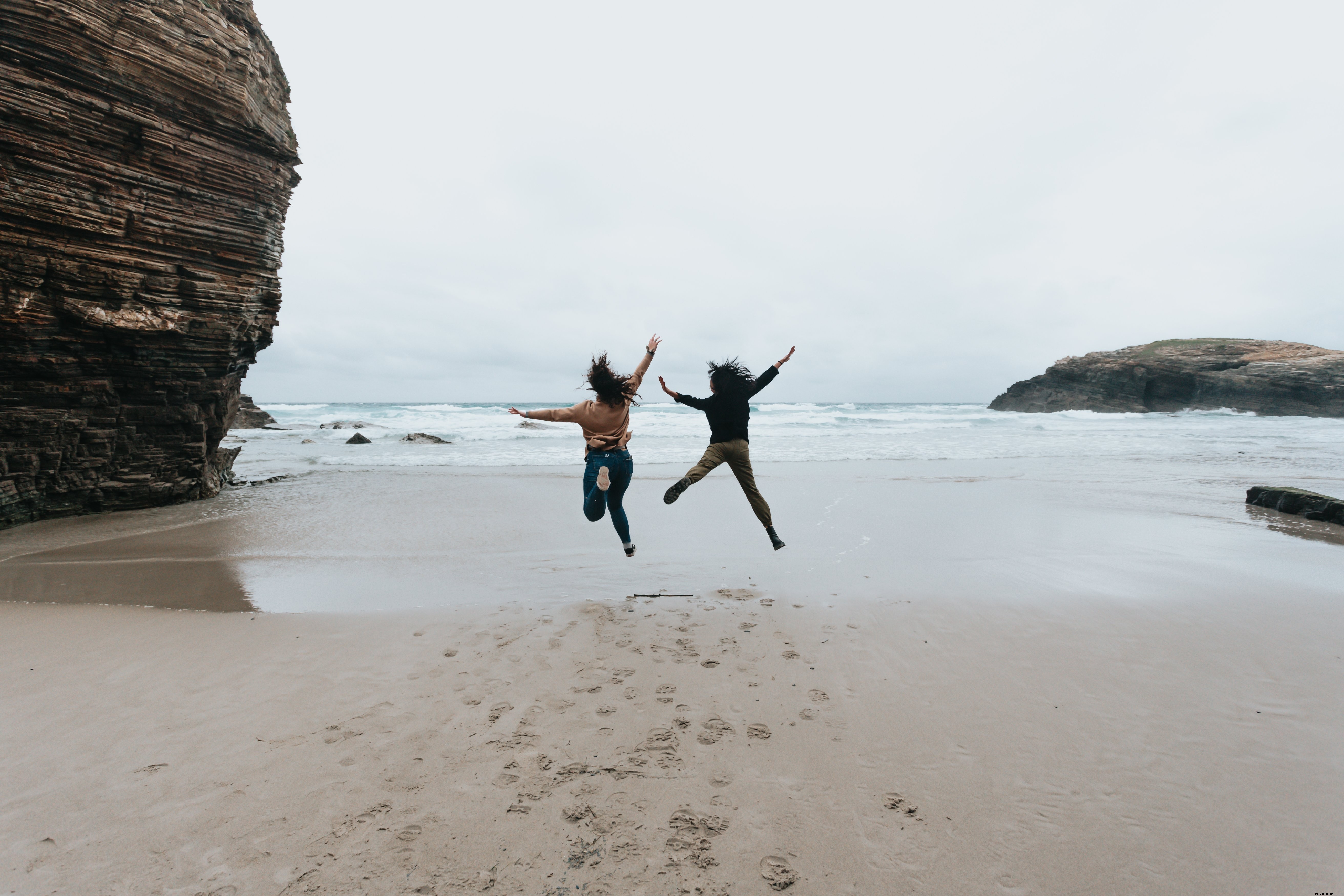 Two People Leaping High on a Pristine Sandy Beach – Stunning Action Photo
