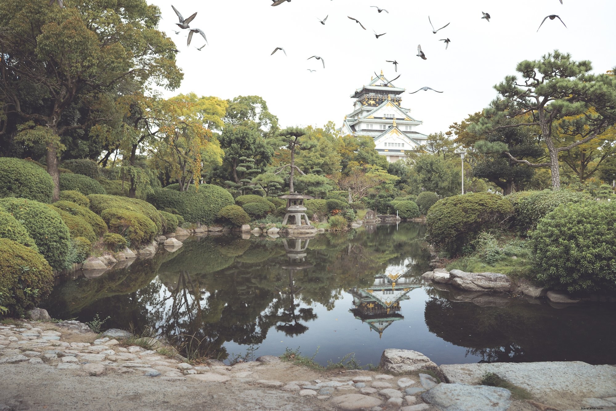Serene Stone-Lined Pond Reflects Majestic White and Gold Building Amid Trees – Stunning Photo