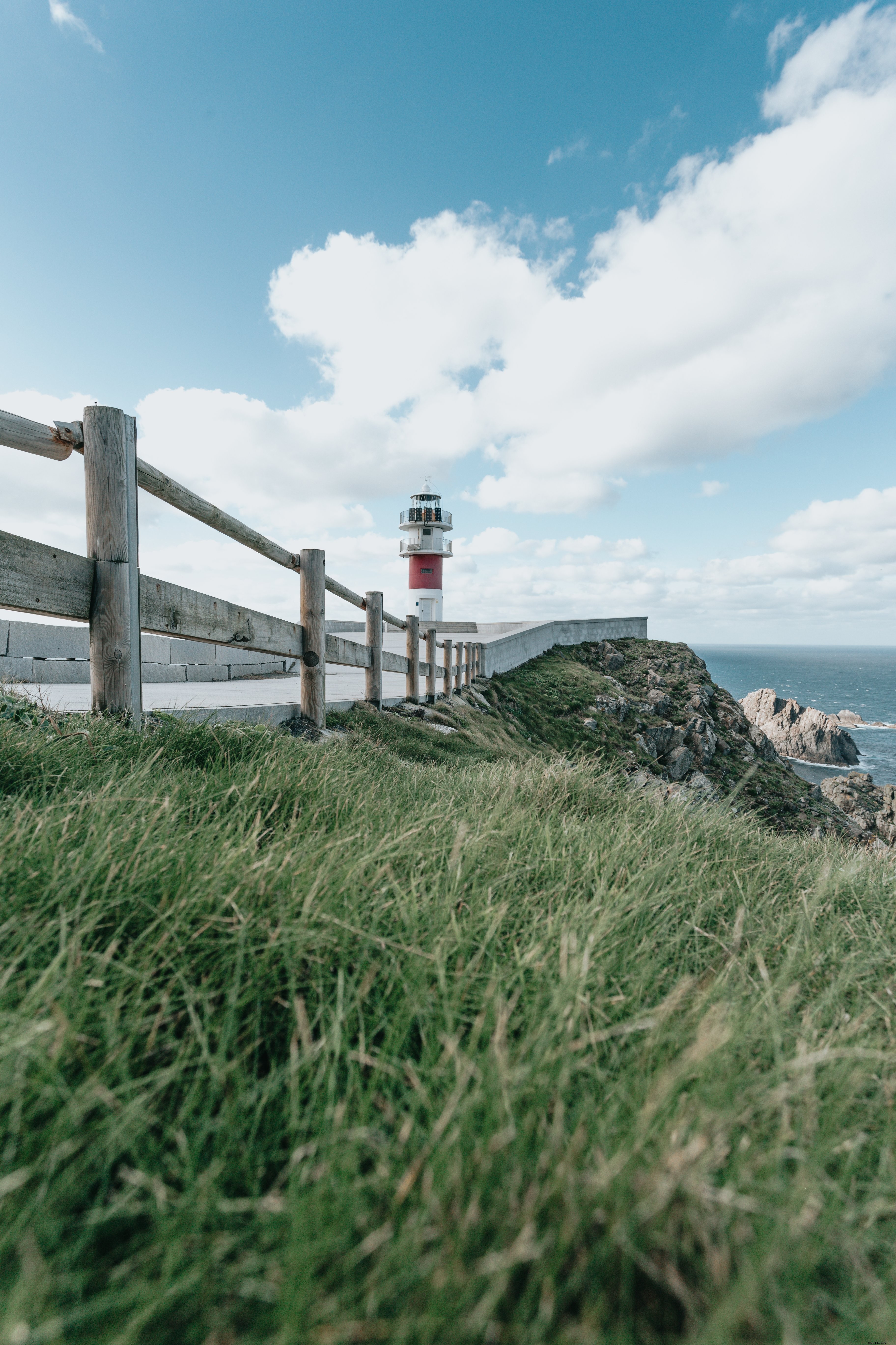 Stunning Green Meadow, Wooden Fence, and Distant Lighthouse – A Captivating Outdoor Scene