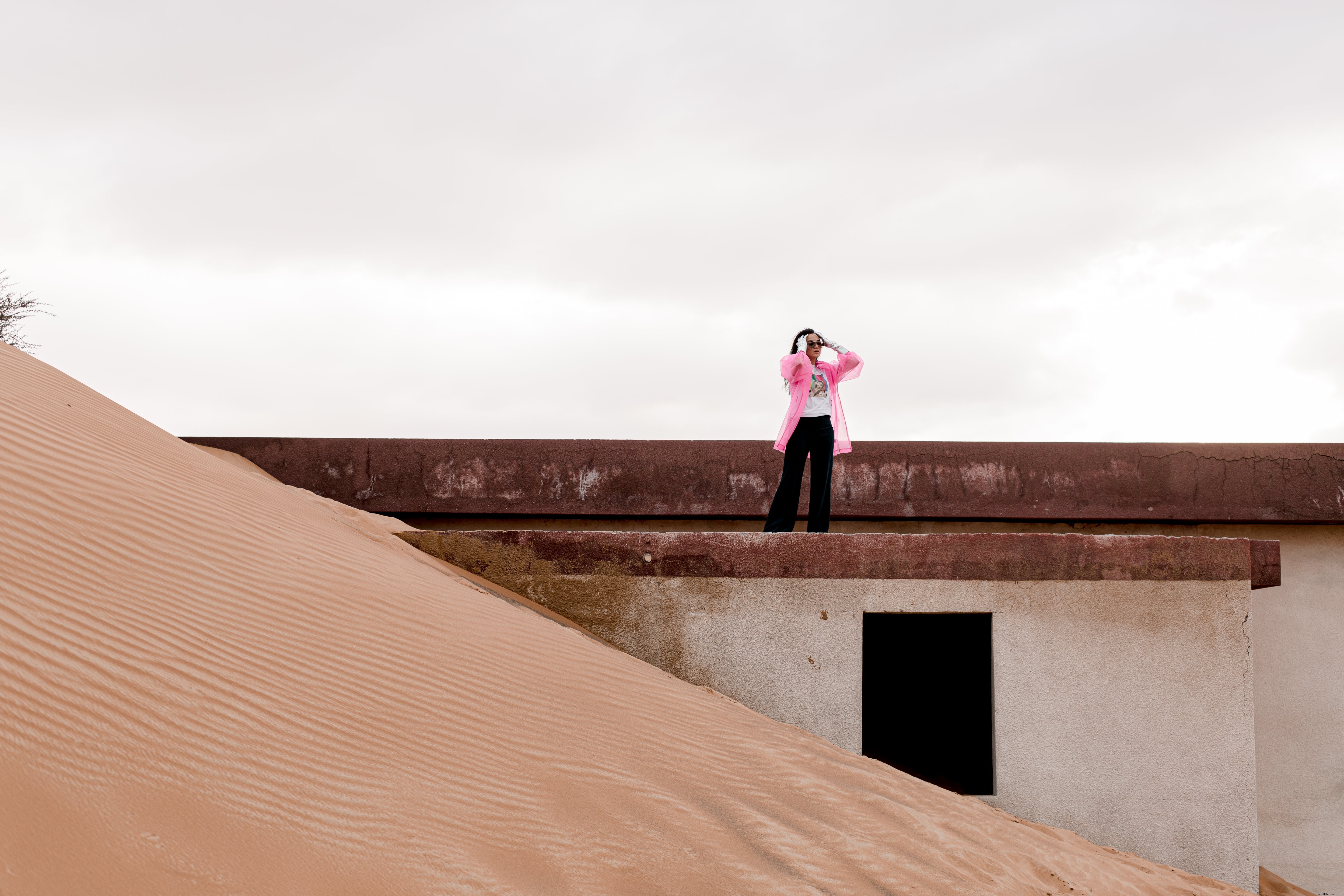 Stunning Photo of Person in Pink Jacket Standing on Sand-Covered Building