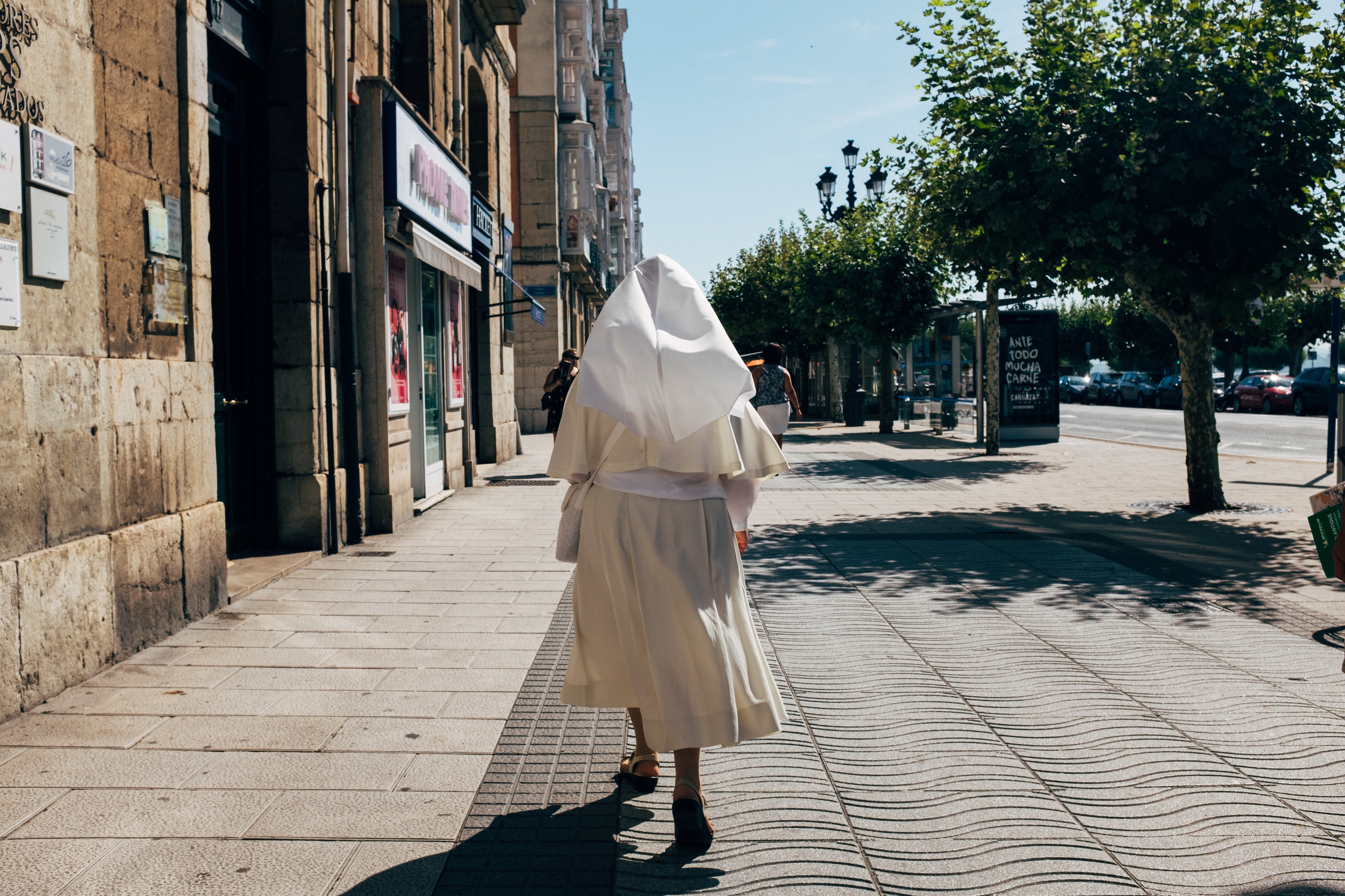 Serene Walk: A Nun in White Habit Strolls Along a Sunny Pedestrian Path