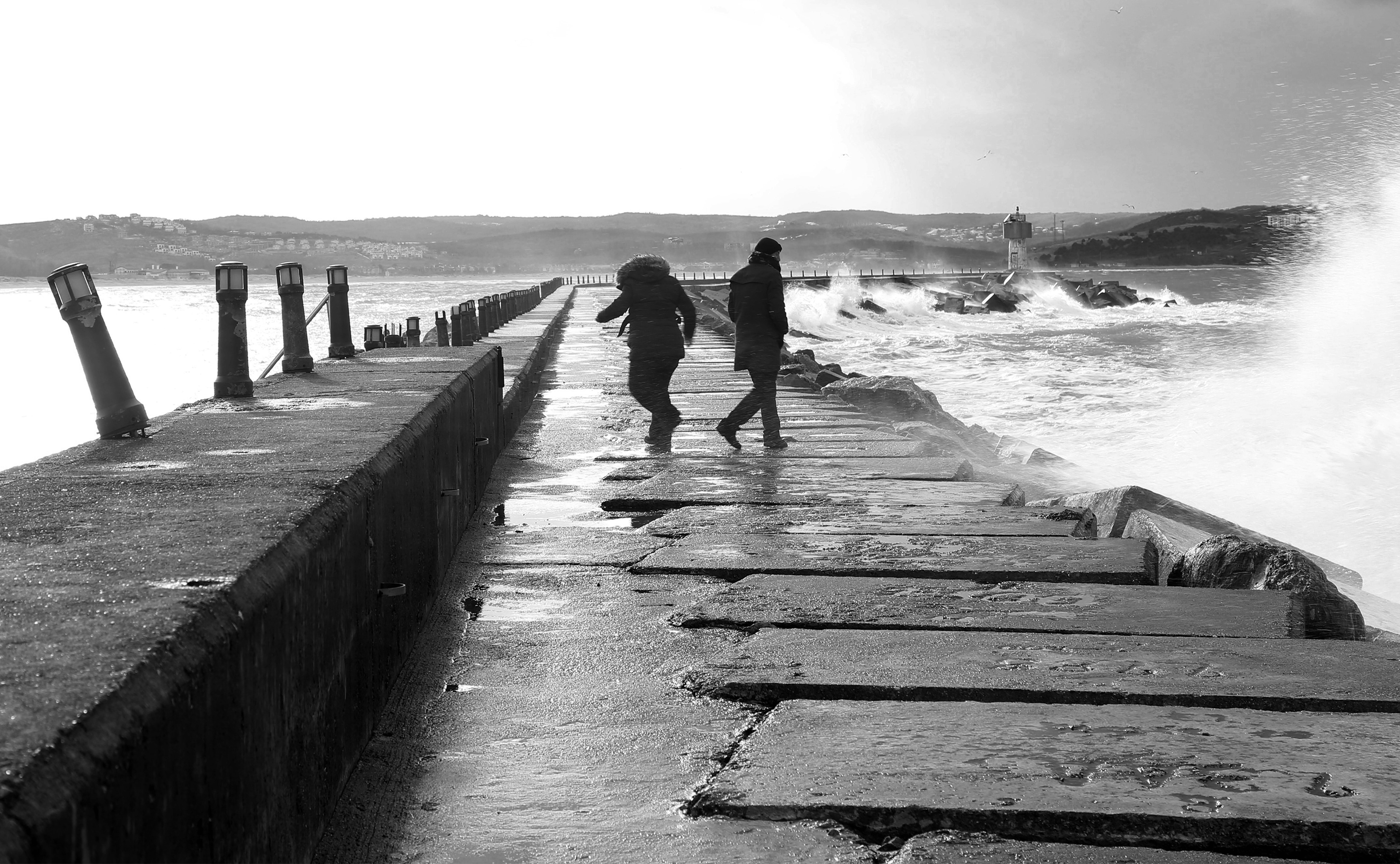 Monochrome Moment: Two People Walking Along Turbulent Ocean Tides