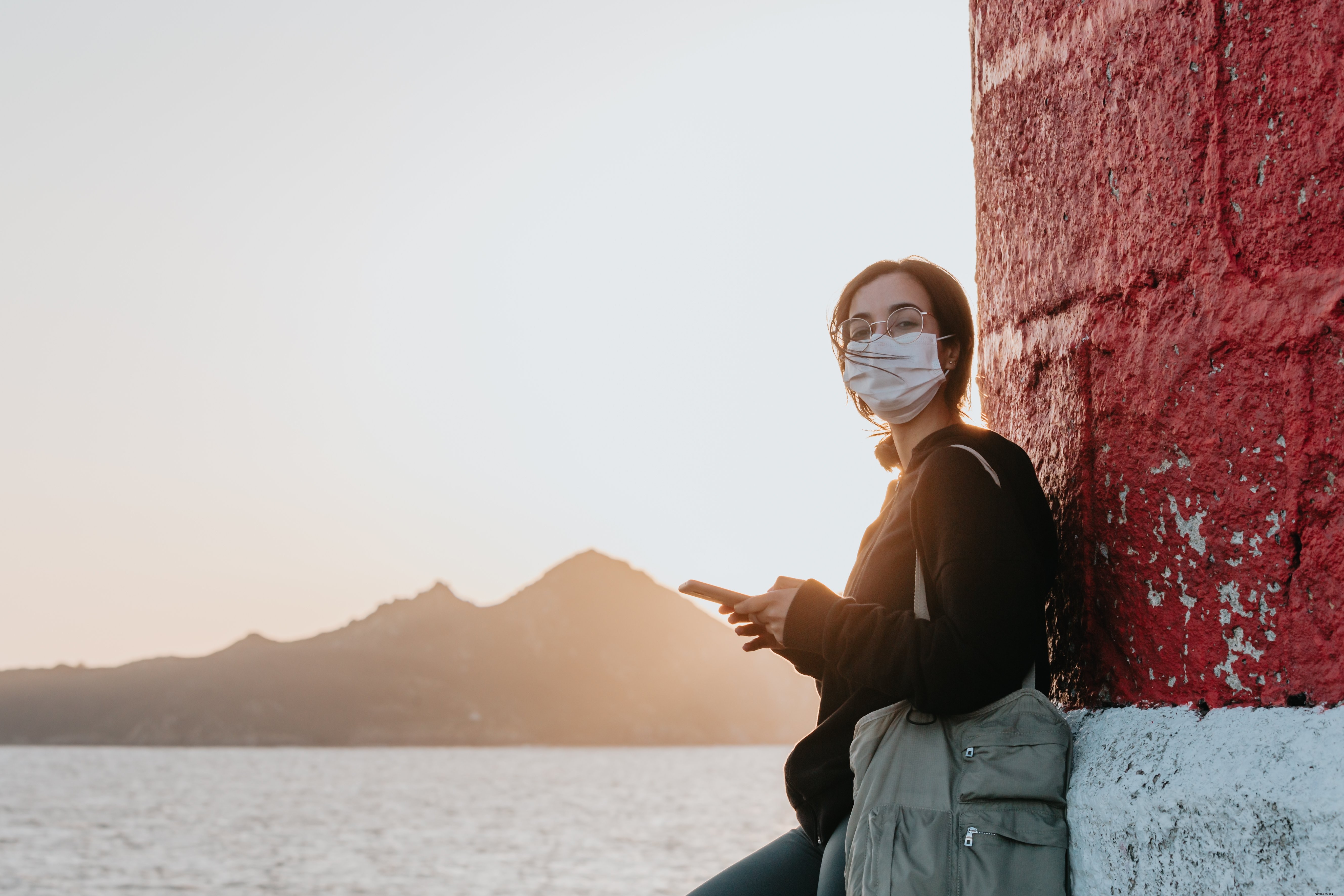 Woman in Face Mask Leaning Against a Wall by the Water – Photo
